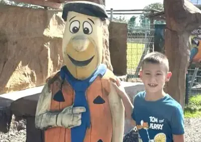 Boy in a blue shirt posing with a pumpkin-themed costume character at an outdoor park or playground, both smiling.